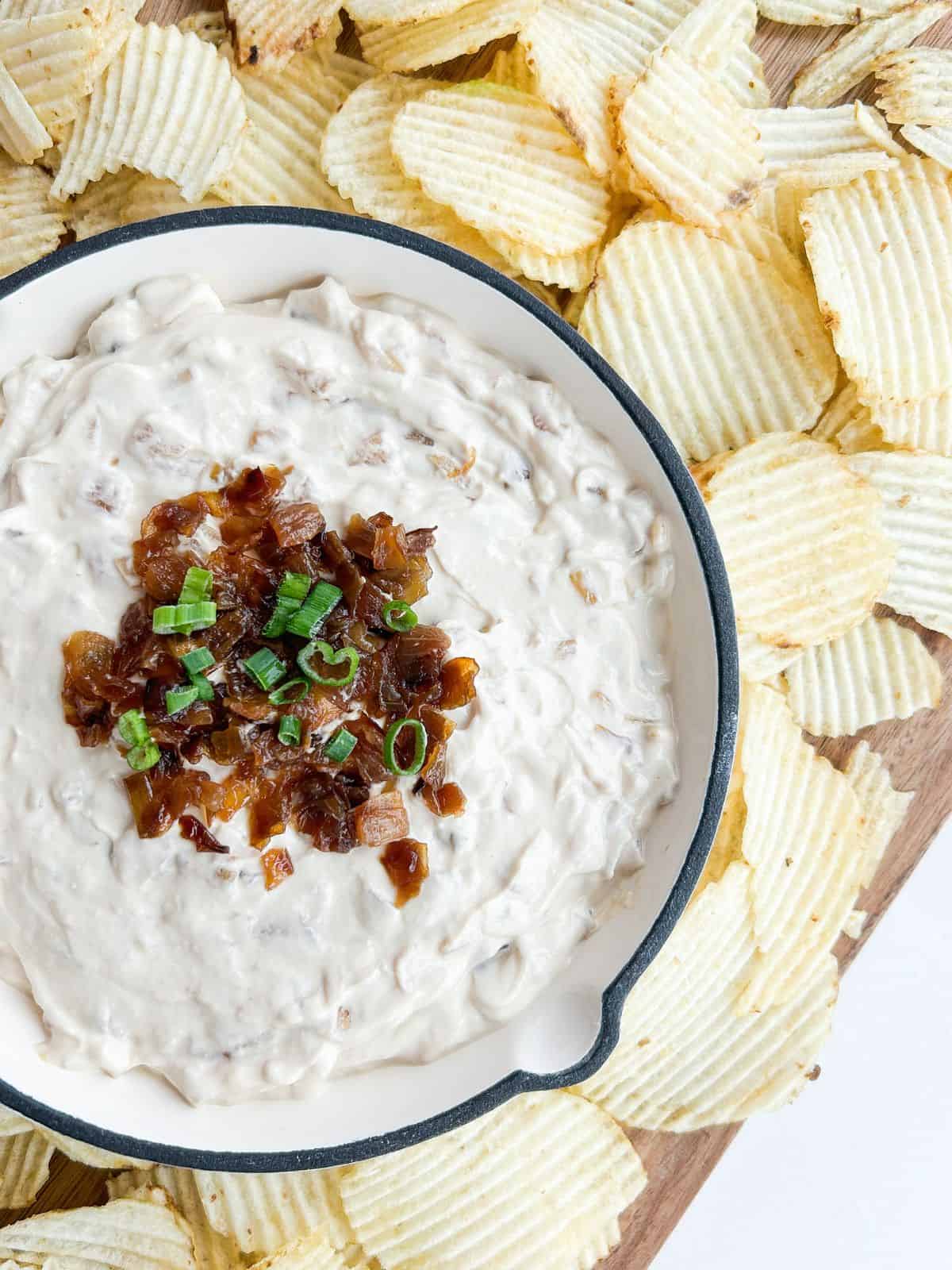 Overhead shot of french onion dip surrounded by ruffled potato chips on a wooden board.