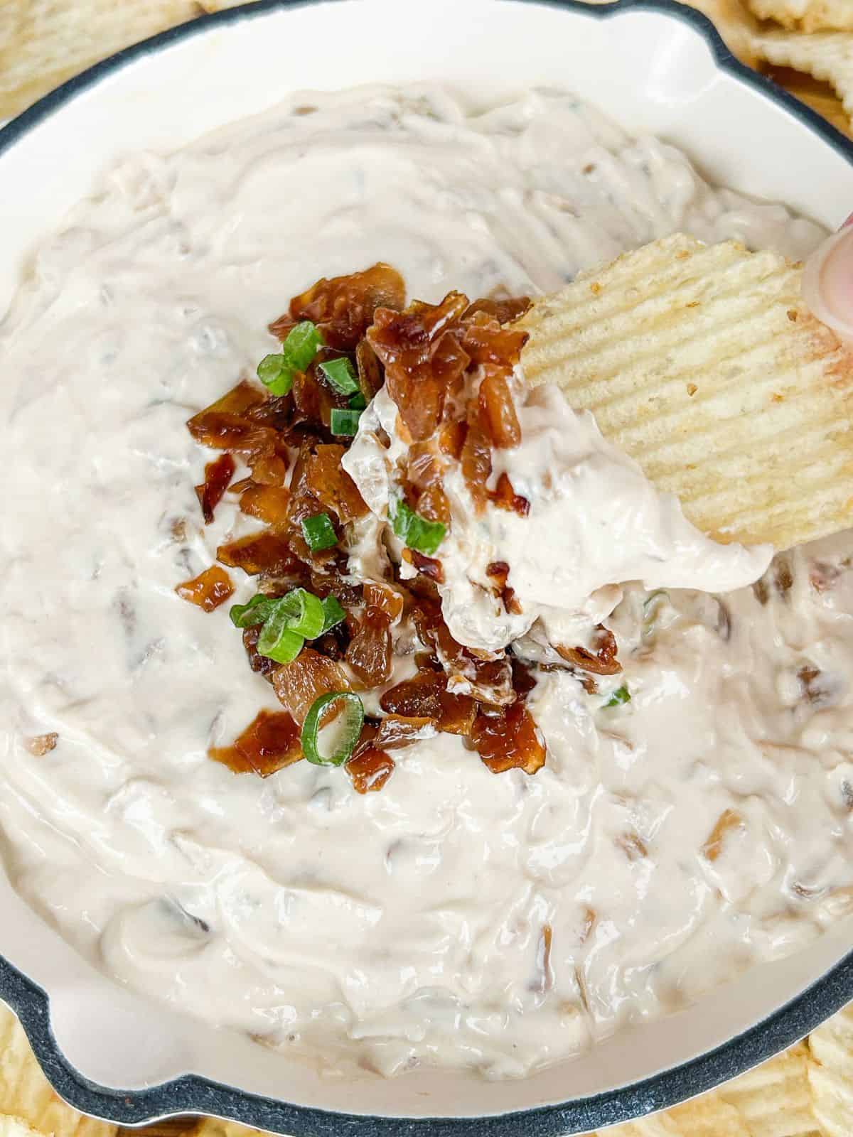 Hand dipping a potato chip into the bowl of French onion dip.