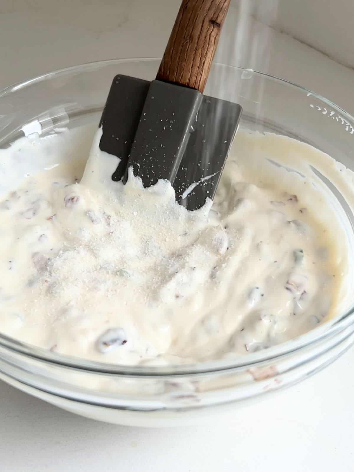 Adding salt to the mixed French onion dip in a bowl with a rubber spatula.