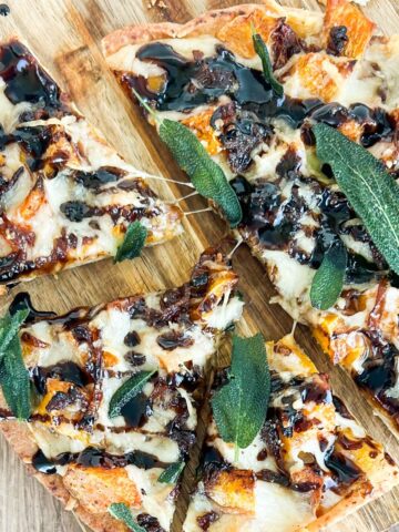 Overhead shot of butternut squash flatbread cut into slices on a wooden background.