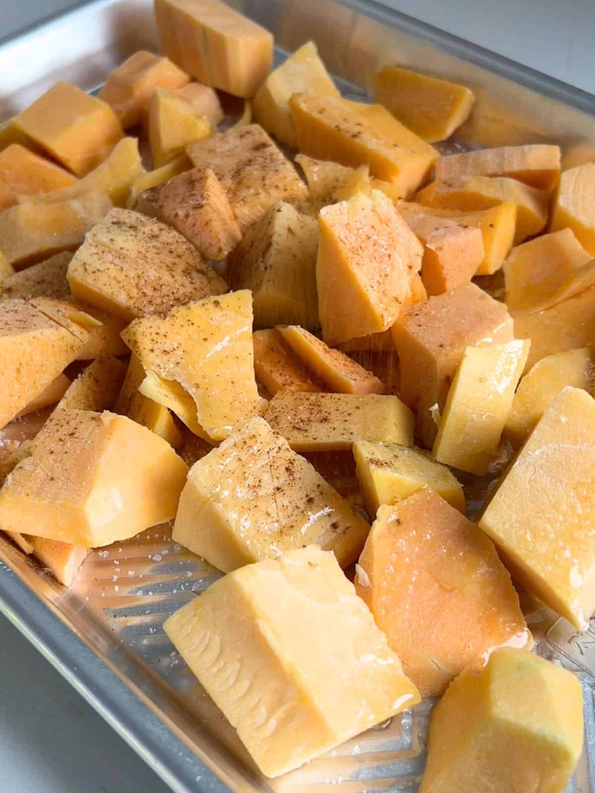 Butternut squash cubes seasoned and drizzled with olive oil on a sheet pan.