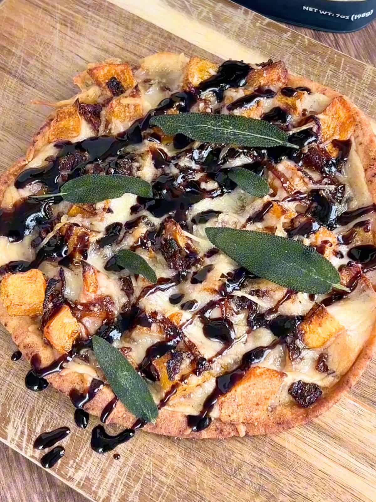 Baked butternut squash flatbread with a balsamic glaze on top on a wooden board.