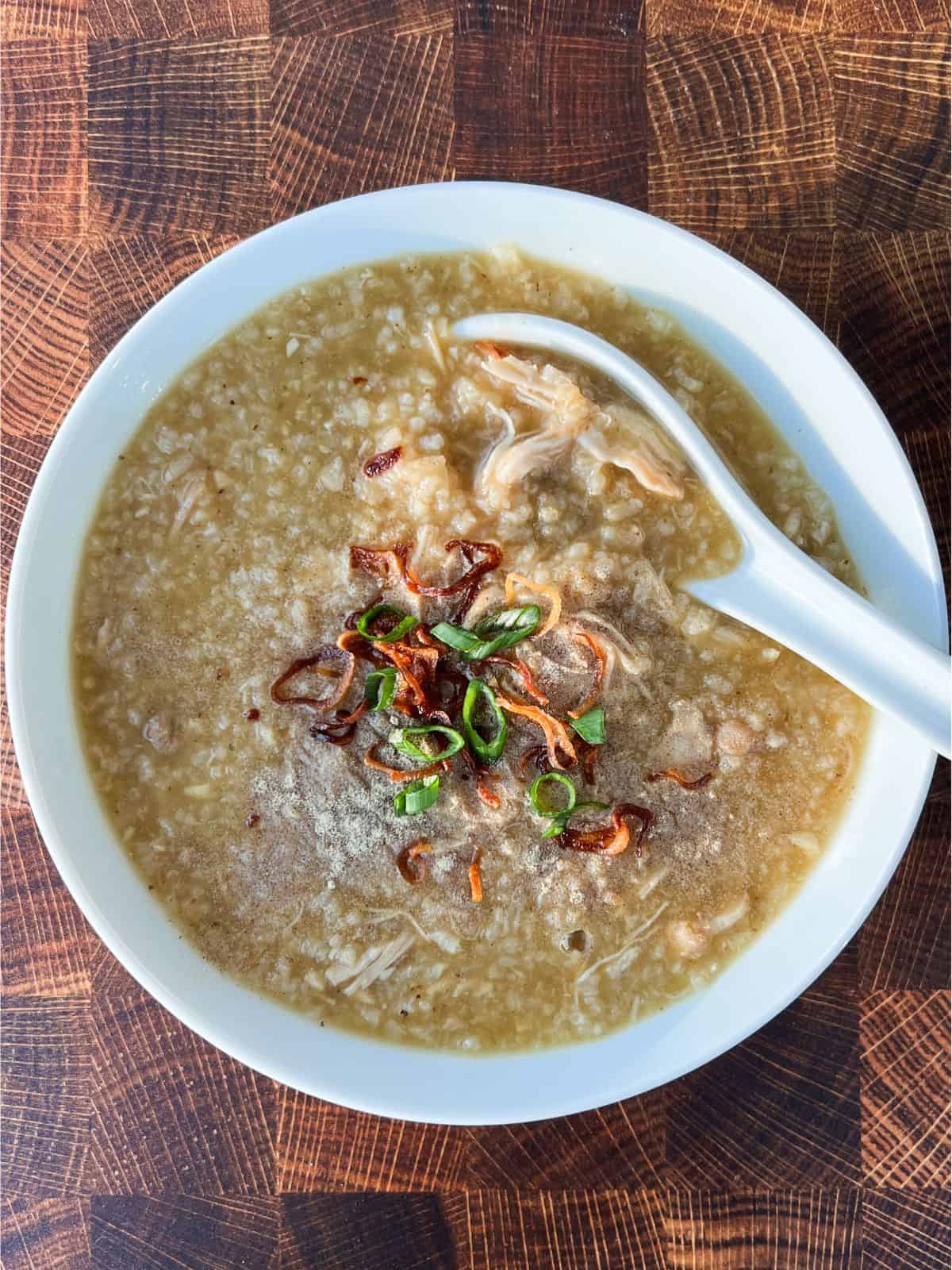 Overhead shot of ginger chicken congee topped with fried shallots and fresh scallions.