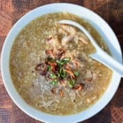 Overhead shot of ginger chicken congee in a white bowl with fried onions on top.