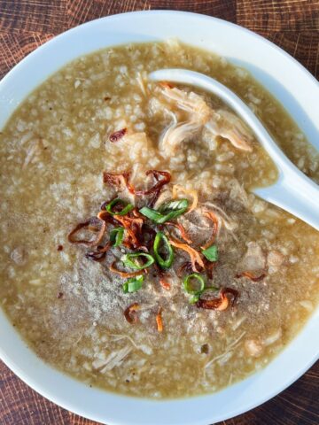 Overhead shot of ginger chicken congee in a white bowl with fried onions on top.