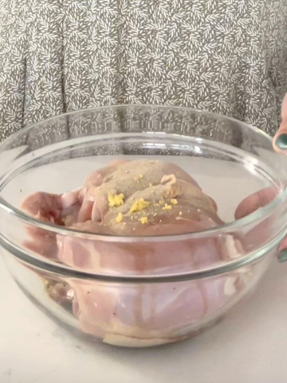 Chicken thighs being marinated in a glass mixing bowl.