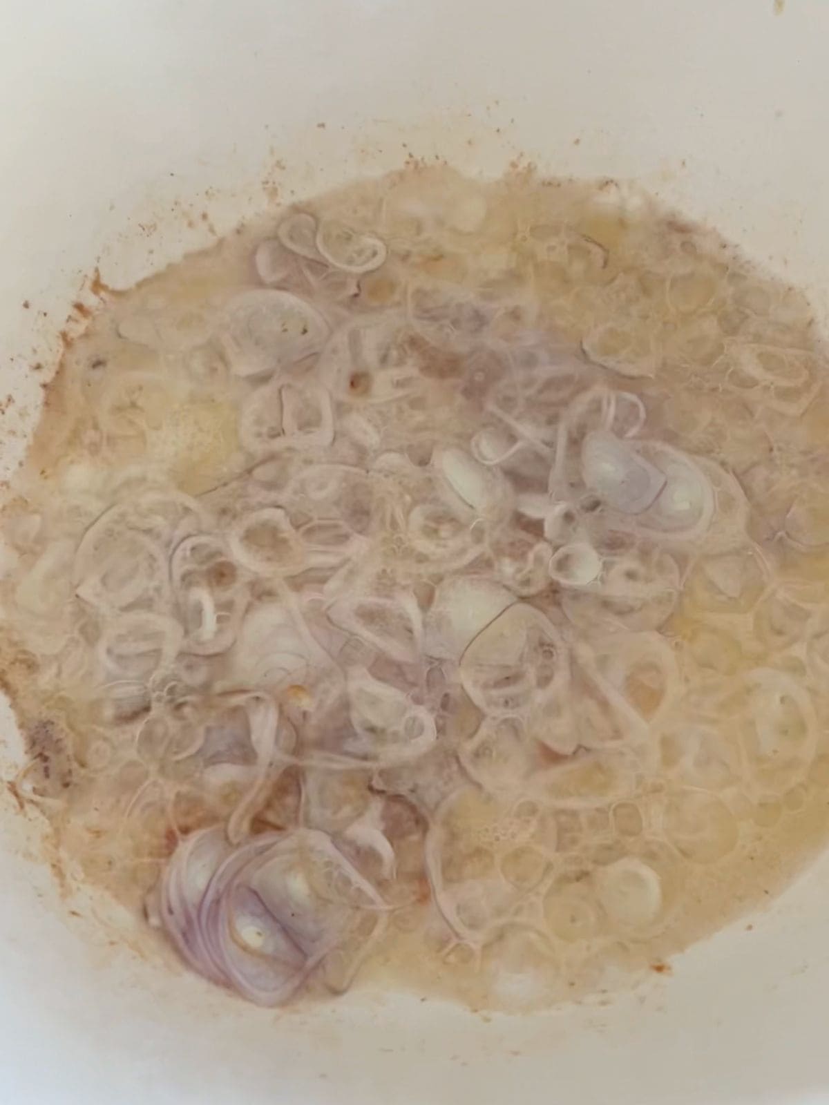 Thinly sliced shallots being fried in chicken fat in a pot.