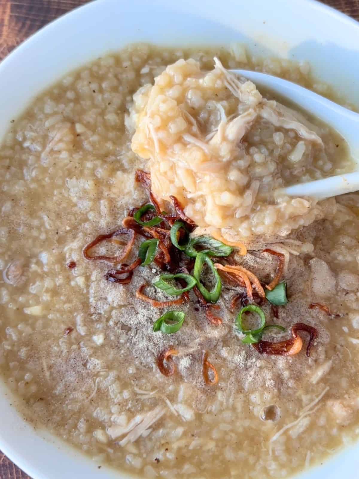 Spoon scooping up some of the ginger chicken congee from a bowl.