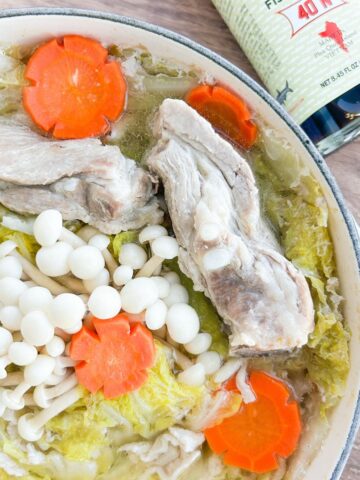 Overhead shot of Vietnamese mille feuille nabe in a Dutch oven next to a bottle of fish sauce.