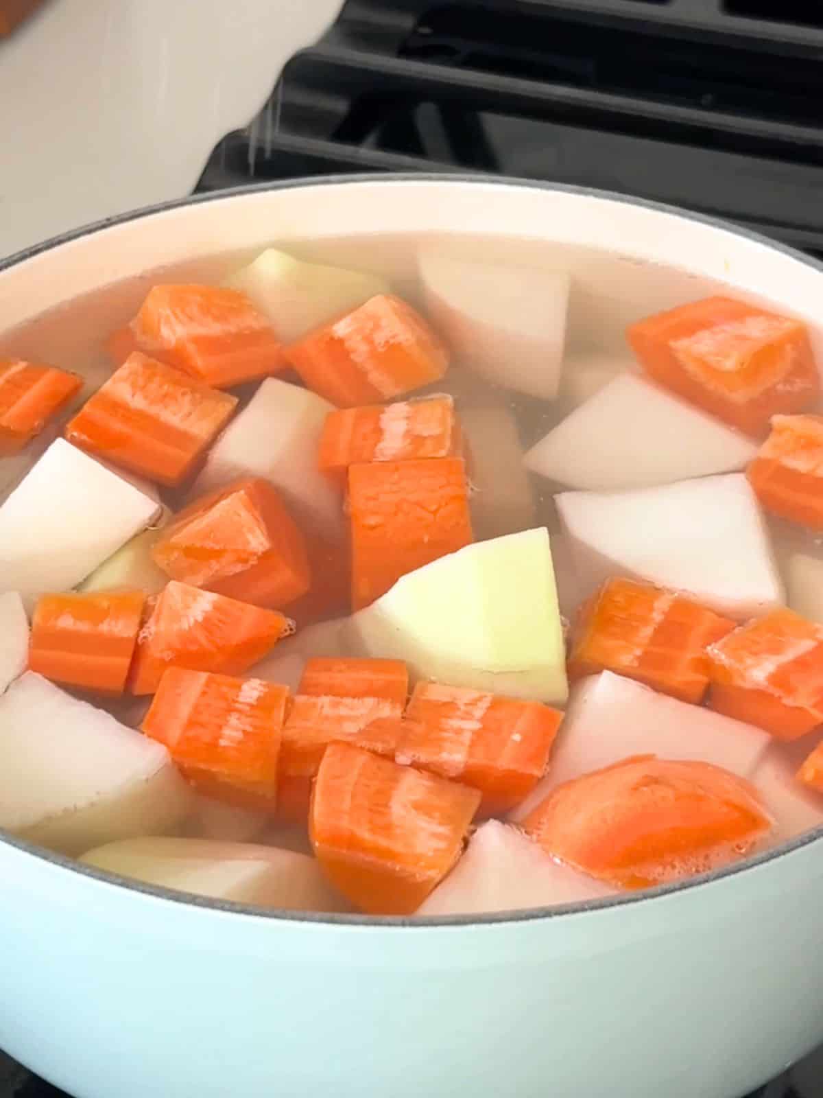 Carrots and diakon radishes cooking in water in a Dutch oven.