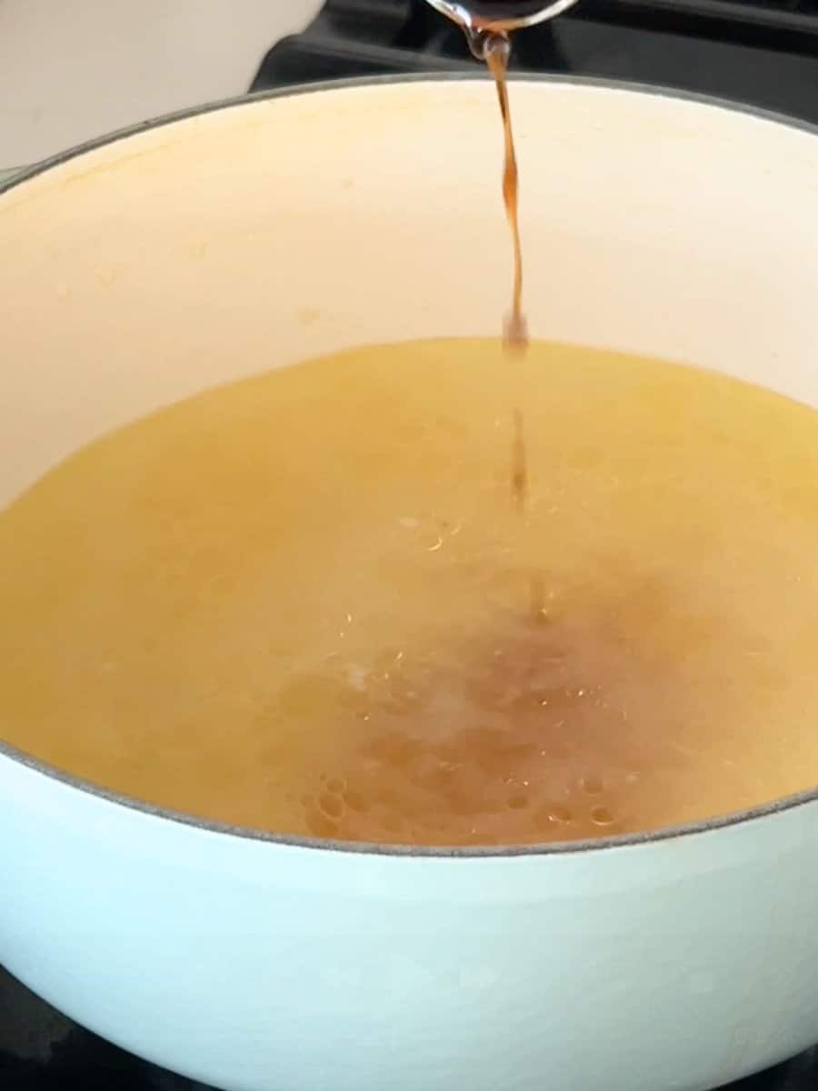 Adding fish sauce to the broth in a large pot.