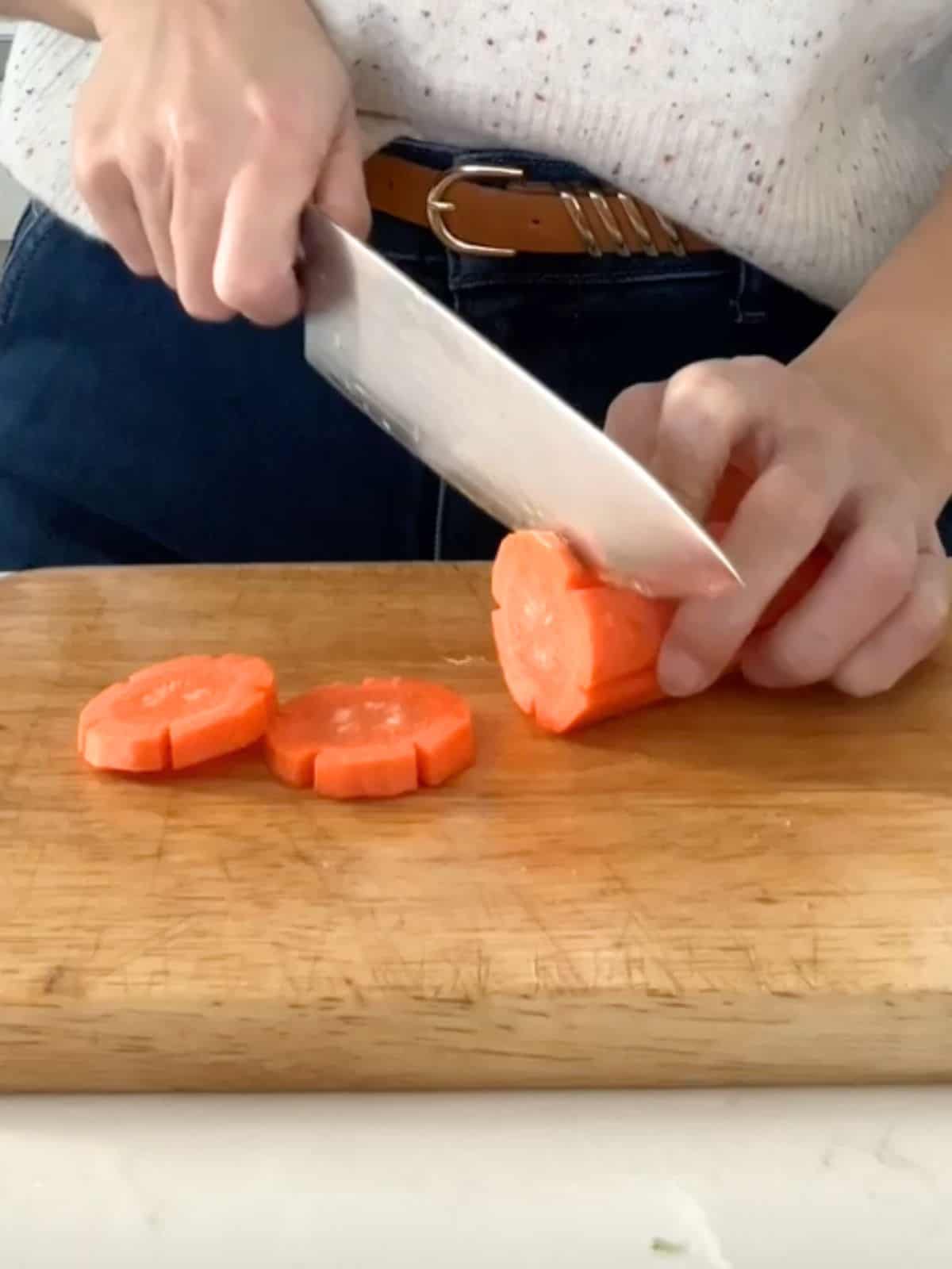 Thinly slicing a large carrot on a wooden board.