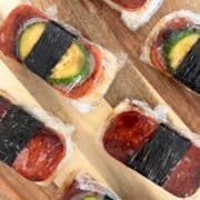 Overhead shot of spam musubi assembled and wrapped in plastic wrap on a wooden board.