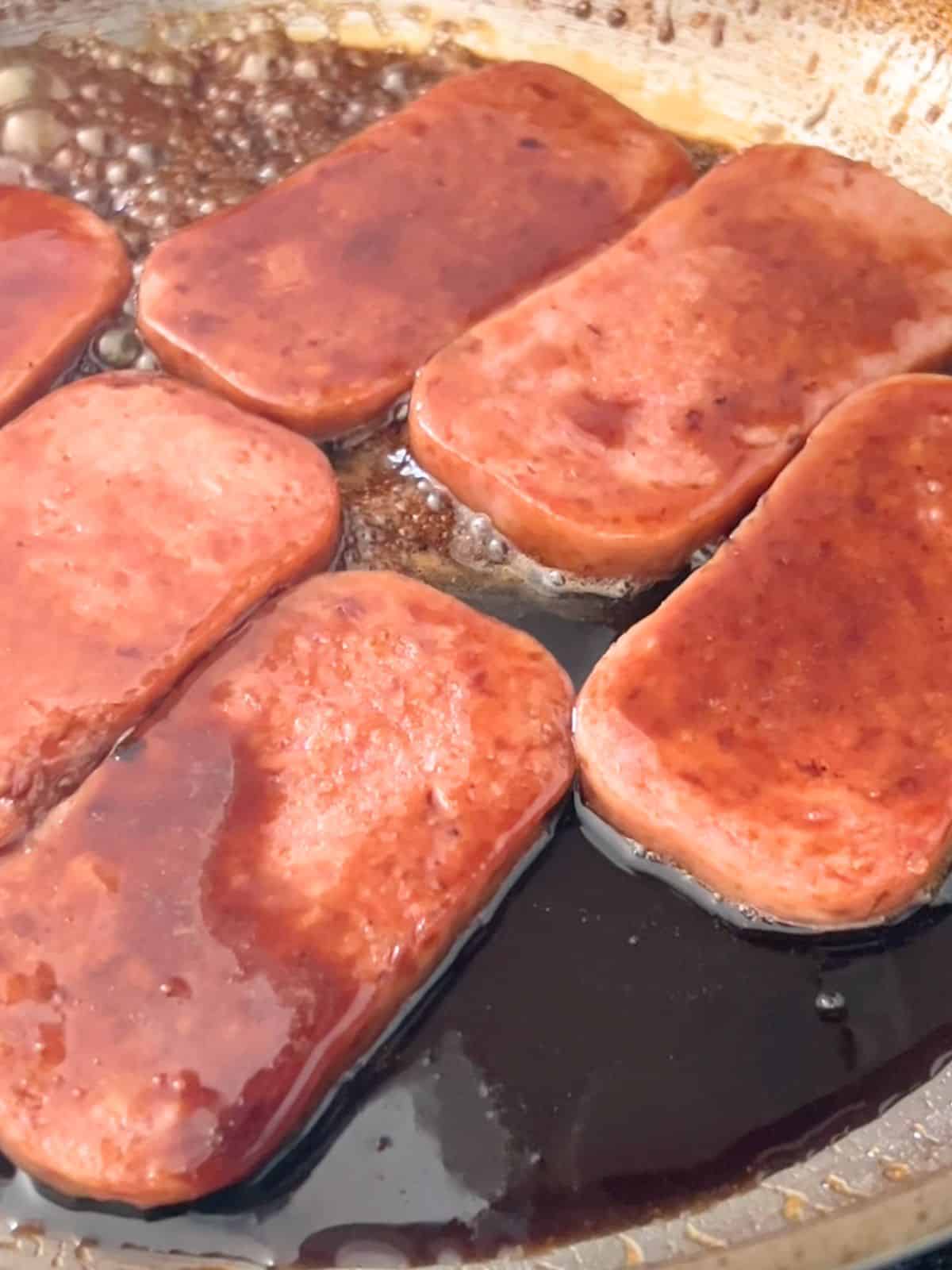 Spam cooking in a soy sauce glaze in a pan.