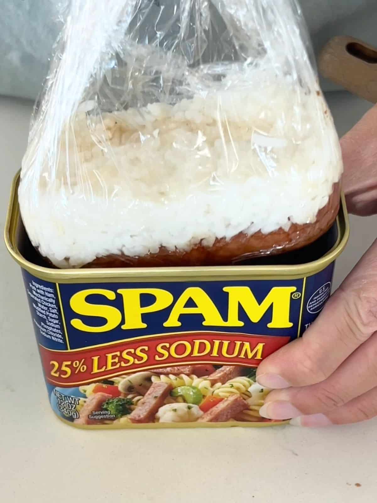 Layers of spam and rice in a plastic wrap being taken from the spam can.