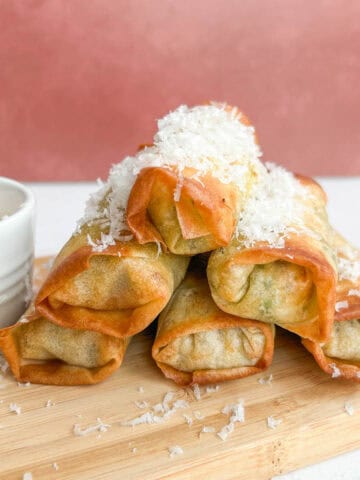 A side shot of the egg rolls stacked on top of each other and garnished with shaved Parmesan cheese.