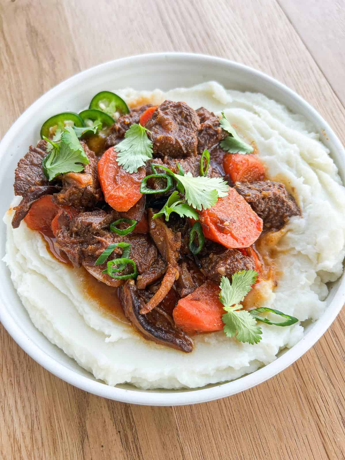 Lemongrass beef stew served in a shallow bowl on a bed of mashed potatoes.