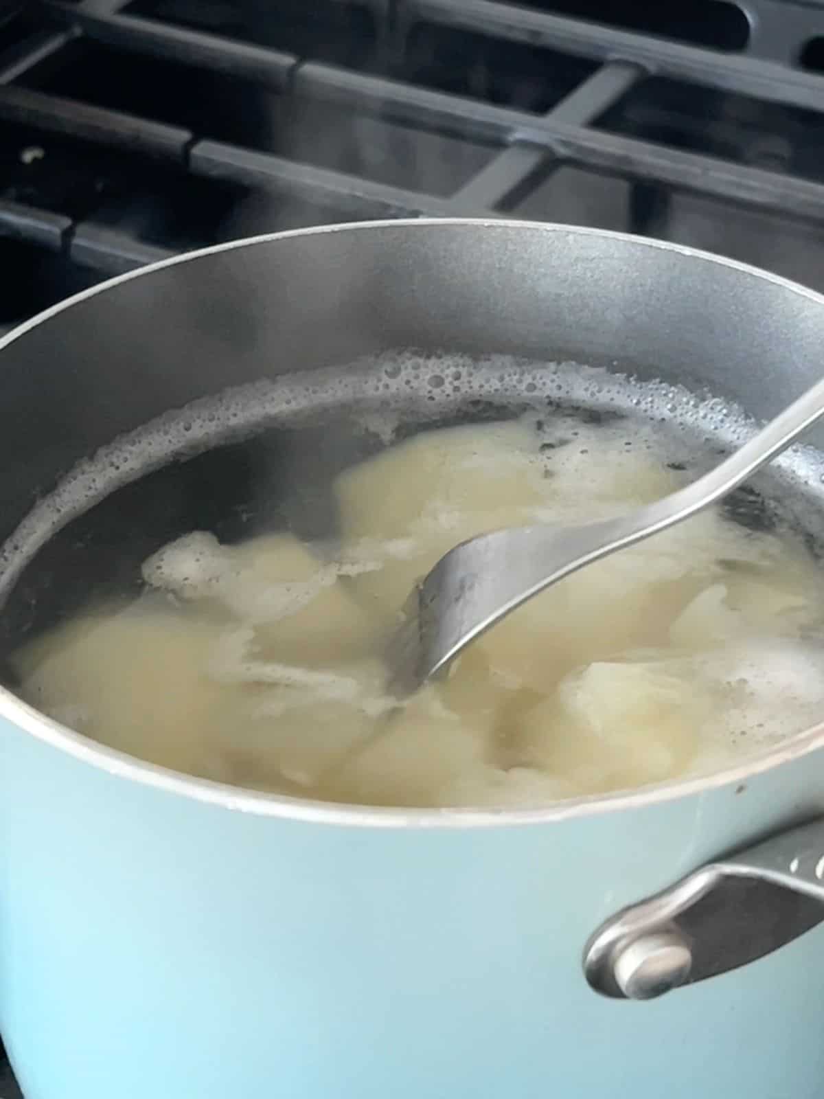 Using a fork to check the boiling potatoes in a pot of water.