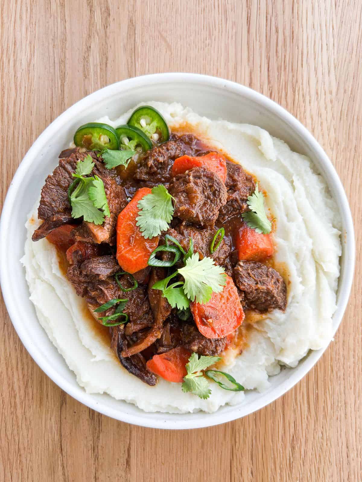 Overhead shot of lemongrass beef stew served on a bed of mashed potatoes.