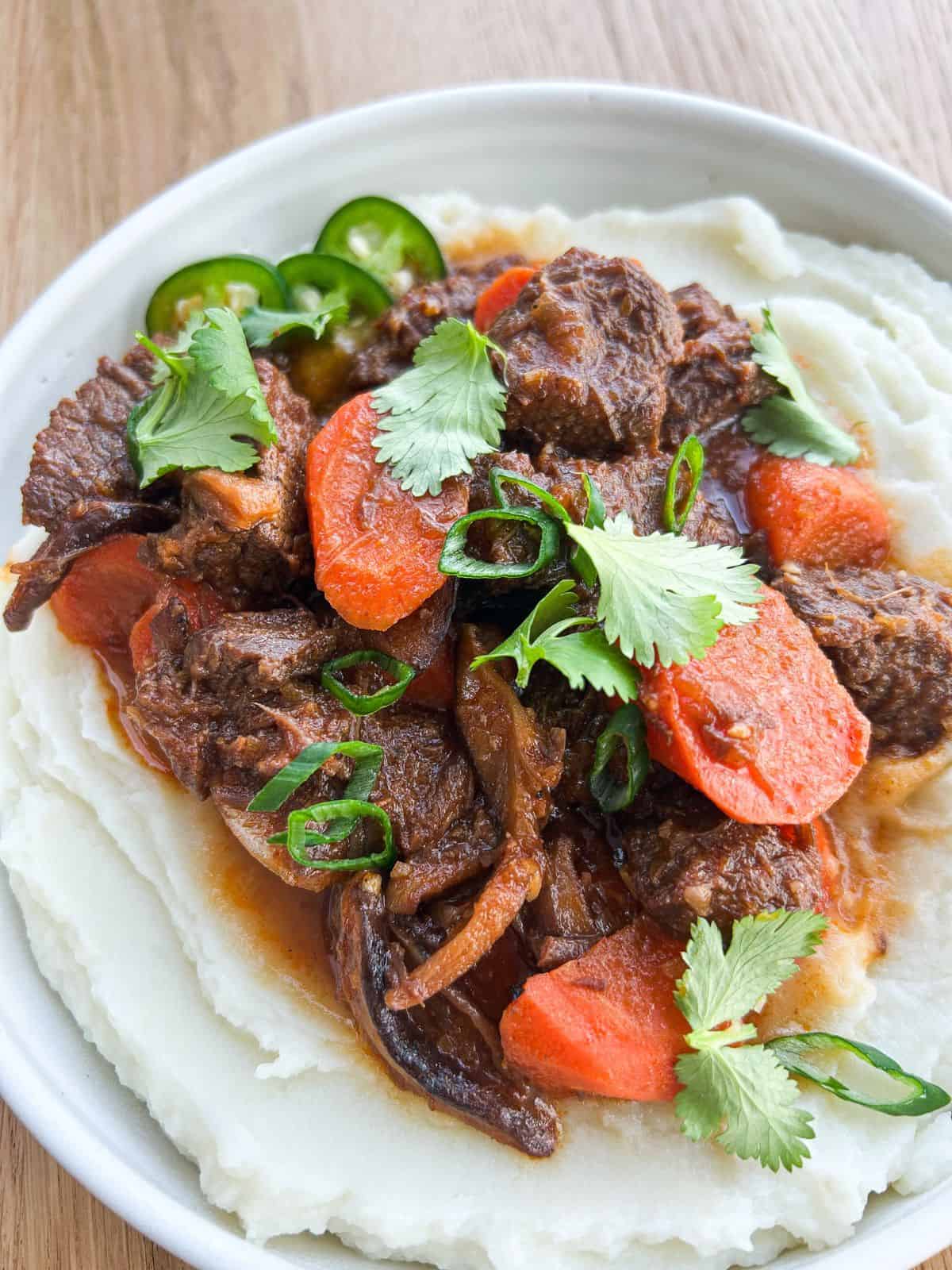 Close up of lemongrass beef stew served on fluffy mashed potatoes.