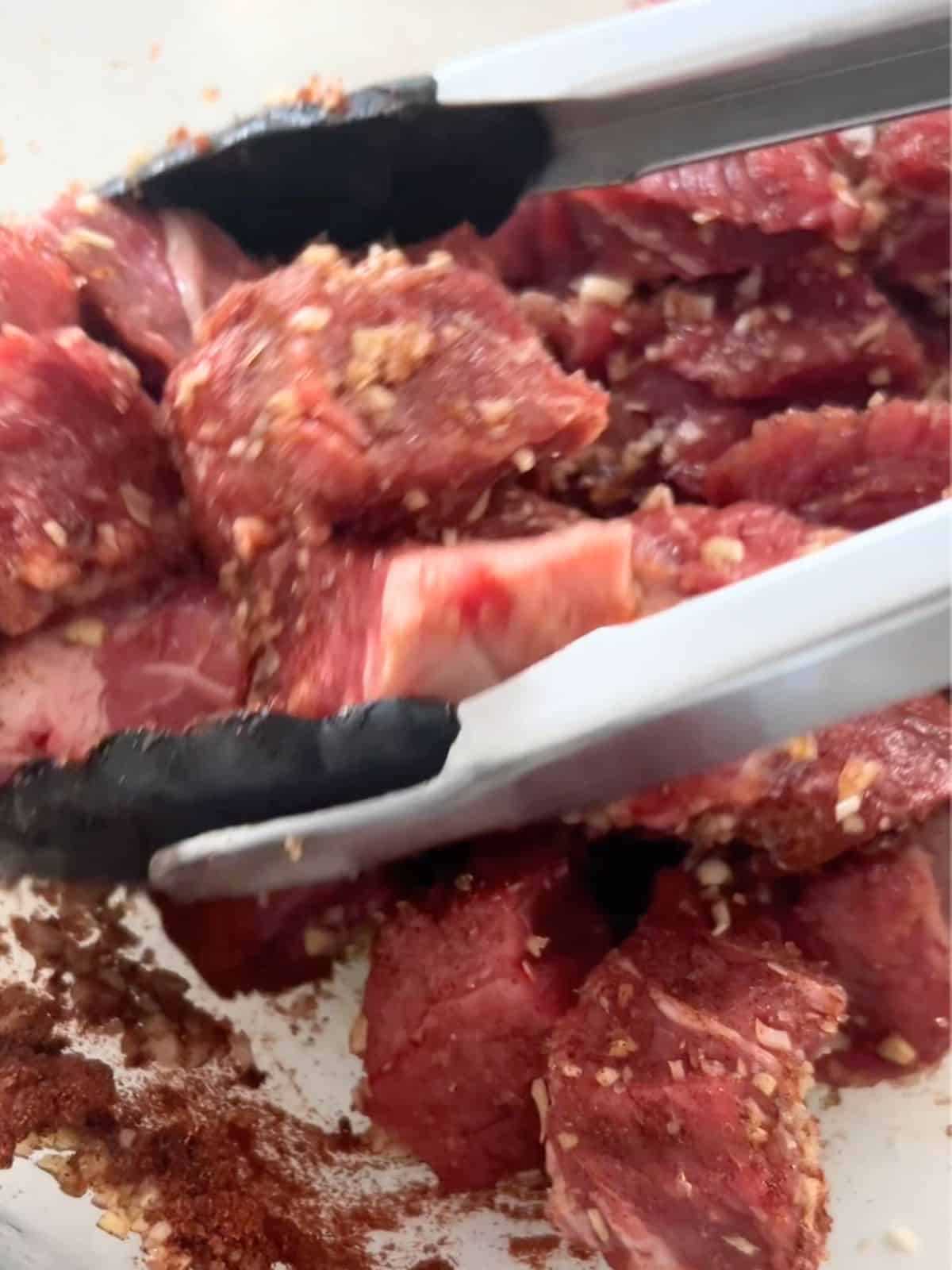 Marinating lemongrass beef stew in a glass bowl and stirring it with tongs.