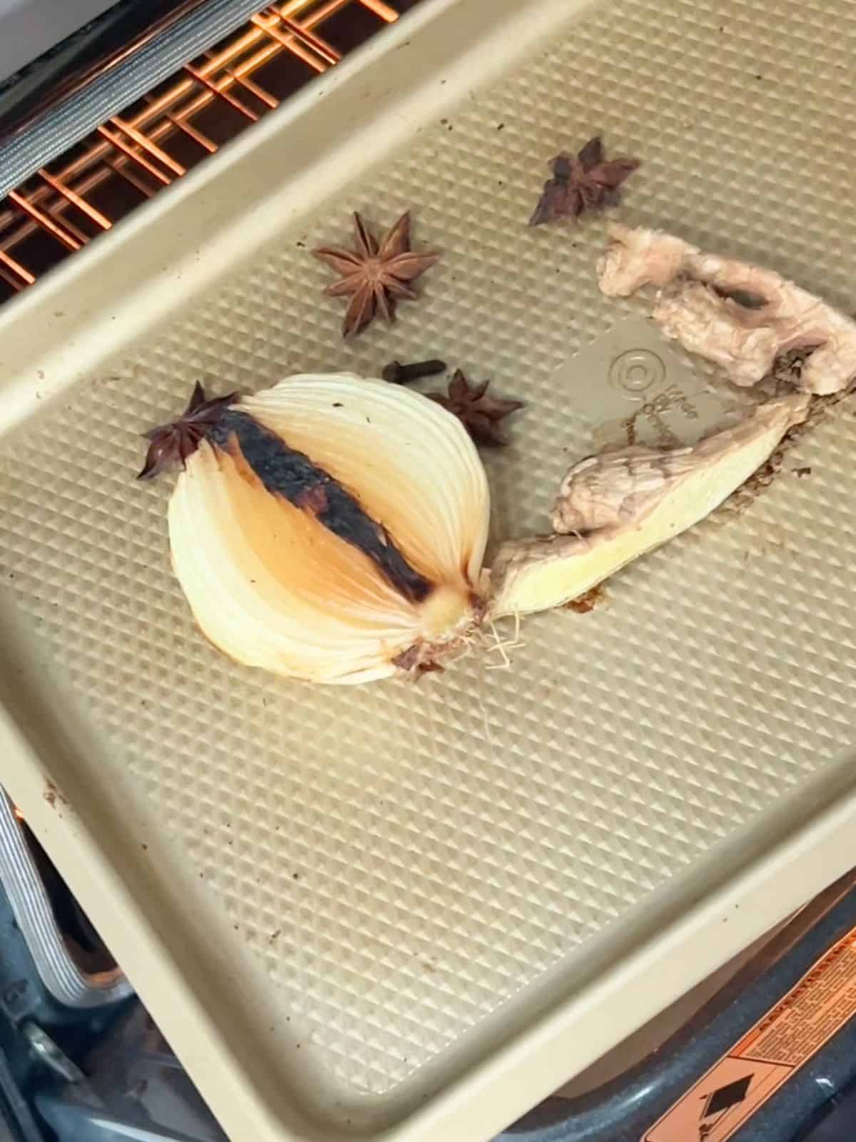 Onions, ginger, cloves and star anise on a sheet pan.