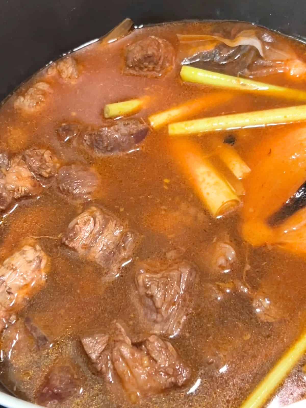 Simmering the beef with lemongrass and toasted spices and onion in a pot.