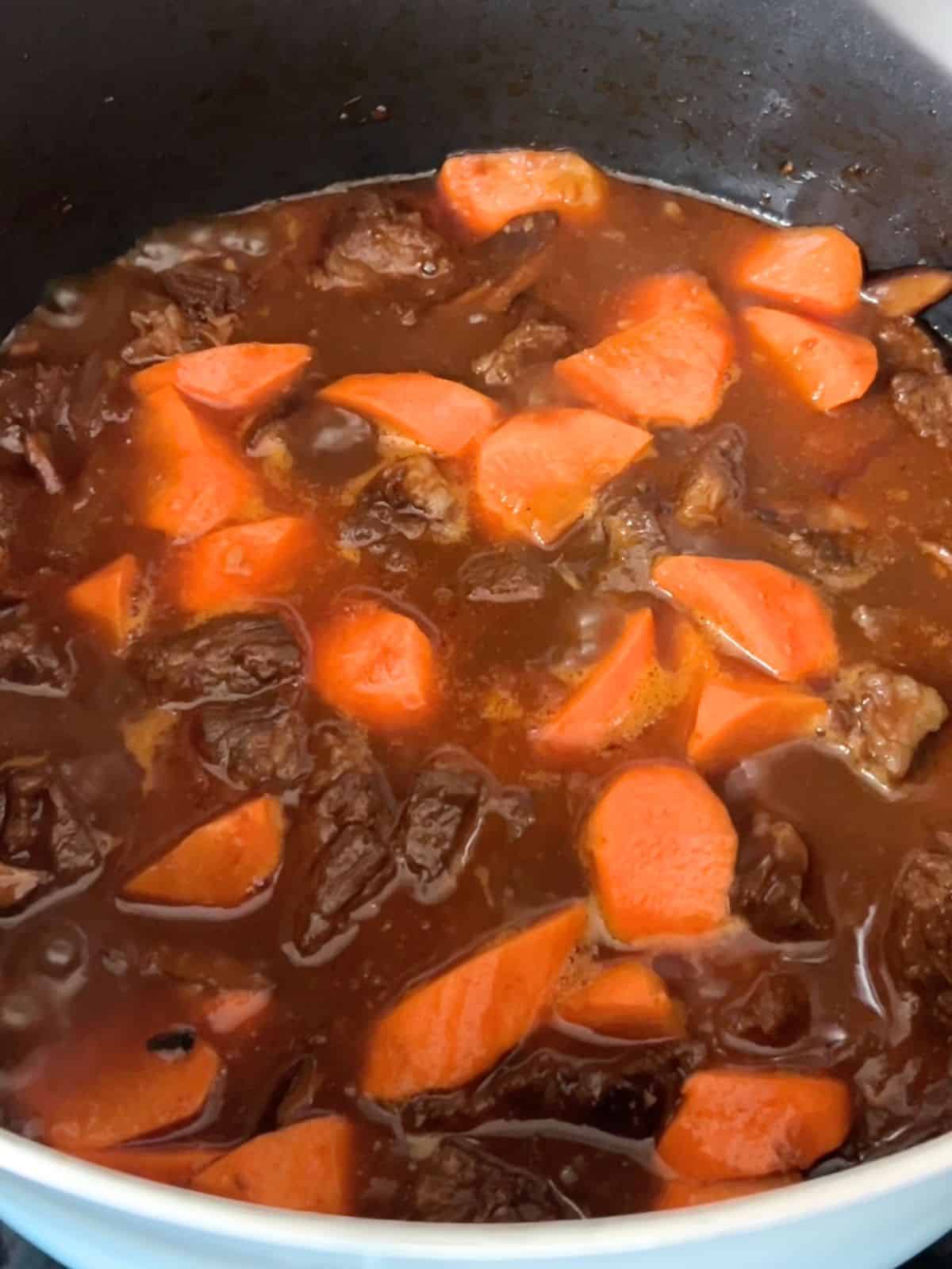 Adding carrots to the simmering beef with broth.