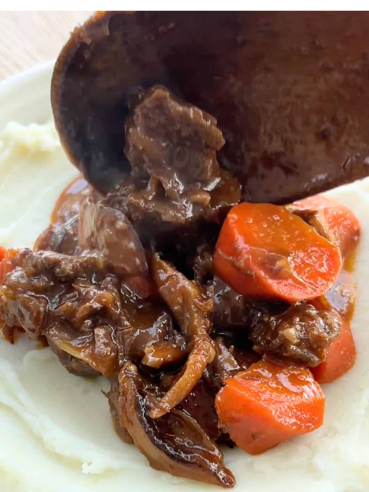 Using a wooden spoon to serve the beef on top of a bed of mashed potatoes.